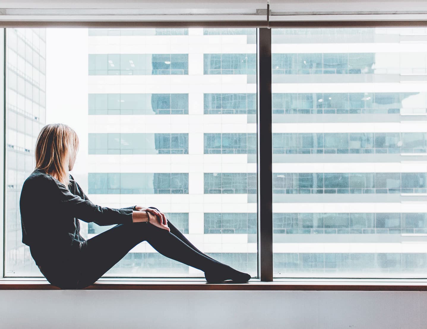 Person sitting on windowsill looking at city